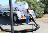 The image shows a large white tanker truck parked in a parking lot. The truck has a large tank on the back with the word "SLU...