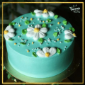 The image is of a round cake with a light blue frosting. The cake is placed on a green cake stand with a gold border. On top...