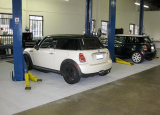 The image shows a garage with two cars parked on lifts. The garage has a concrete floor and white walls. There are two blue p...