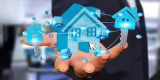 The image shows a person's hand holding a blue house-shaped icon. The house is made up of small blue icons that represent dif...