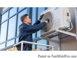 In this image, we can see a man working on an outdoor air conditioning unit. He is wearing a blue uniform and is standing on...