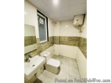The image shows a small bathroom with a white tiled floor and walls. On the left side of the image, there is a white sink wit...