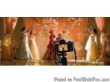 The image shows a wedding scene with a camera on a tripod in the foreground. The camera is positioned in front of a stage wit...