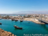 The image is a beautiful landscape of a coastal area with a clear blue sky and mountains in the background. The water is a de...