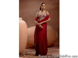 The image shows a young woman wearing a traditional Indian saree. She is standing in front of a large vase and a large pot, w...