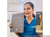 The image shows a young woman in a blue scrub top holding two books in her hands. The books are titled "Amitabh Shubhoo Mishr...