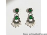 The image shows a pair of earrings. The earrings are made of silver and have a teardrop-shaped design with a green stone in t...