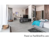 The image shows a modern and luxurious bedroom with a large bed on the right side of the room. The bed has a blue and white c...