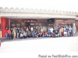 The image shows a group of people standing in front of a building with a red awning. The building appears to be a restaurant...