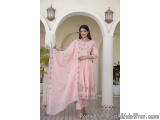 The image shows a young woman wearing a traditional Indian outfit. She is standing in an archway with white columns and two l...