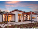 The image shows a modern, two-story house with a unique design. The house has a white exterior with a sloping roof and large...