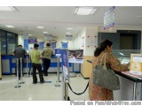 The image shows the interior of an airport check-in counter. There are several people standing in front of the counter, which...