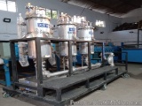 The image shows a large industrial machine in a warehouse. The machine is made of stainless steel and has a cylindrical shape...
