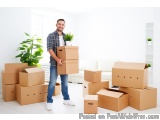 The image shows a young man standing in a room with a pile of cardboard boxes. He is holding a stack of cardboard box in his...