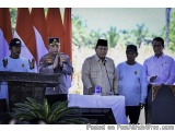 The image shows a group of five men standing behind a podium with Indonesian flags in the background. The man in the center i...