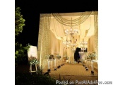The image shows a beautiful and elegant wedding venue at night. The focal point of the image is a large chandelier hanging fr...