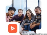 The image shows a group of four young people sitting around a table in a meeting room, looking at a laptop screen. They are a...