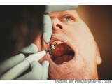 The image shows a close-up of a man's mouth being examined by a dentist. The dentist is wearing a green glove and is holding...