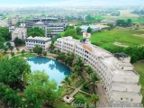 The image is an aerial view of a large, modern building with a swimming pool in the center. The building appears to be a hote...