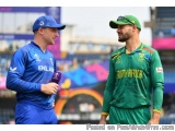 The image shows two men standing on a cricket field, engaged in a conversation. The man on the left is wearing a blue England...