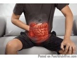 The image shows a man sitting on a couch with his stomach exposed. He is wearing a black t-shirt and black shorts. The stomac...