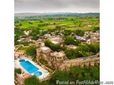 The image is an aerial view of a beautiful village in India. The village is surrounded by green fields and hills, and the sky...