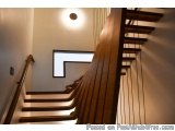 The image shows a wooden staircase in a modern home. The staircase has a curved wooden handrail on the left side and a white...