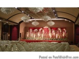 The image shows a large banquet hall with a high ceiling and multiple chandeliers hanging from it. The hall is decorated with...