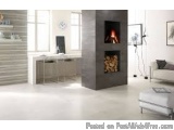 The image shows a modern living room with a fireplace in the center. The fireplace is made of concrete and has a black finish...