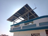 The image shows a building with a large solar panel on top of it. The solar panel is mounted on a metal frame and is supporte...