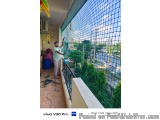 The image shows a man standing on a balcony with a view of a city. He is wearing a green t-shirt and is holding a yellow tool...
