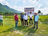 The image shows a group of men standing in front of a large sign that reads "Pamsquare Blossom Valley Run By Development". Th...