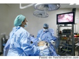 The image shows two surgeons performing an operation in an operating room. They are both wearing blue surgical gowns, masks,...