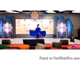 The image shows a stage set up for a performance. The stage is decorated with blue and orange accents and has a large screen...