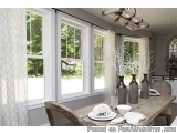 The image shows a dining room with a wooden table and chairs. The table is set with white plates, silverware, and vases with...