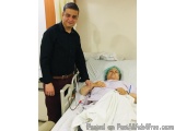 The image shows a man standing next to a hospital bed with a patient lying on it. The patient is wearing a green surgical cap...