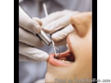 The image shows a close-up of a person's mouth being examined by a dentist. The dentist is wearing white gloves and is holdin...