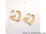 The image shows a pair of gold hoop earrings on a white marble surface. The earrings are in the shape of a heart, with a curv...