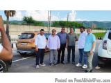 The image shows a group of six men standing in a parking lot. They are all dressed in casual clothes and are posing for a pho...