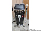 The image shows a black-colored machine with a large screen on top. The machine is labeled "TRITON" and has a handle on the r...