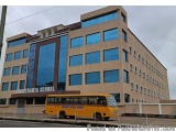 The image shows a large, modern building with a beige exterior and large windows. The building appears to be a school or a hi...