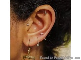 The image shows a close-up of a person's ear. The person has black hair and is wearing a pair of earrings. The earring on the...