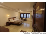 The image shows a modern and spacious bedroom with a large bed in the center. The bed has a wooden headboard and footboard wi...