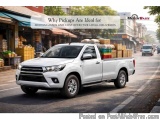 The image shows a white Toyota Hilux pickup truck driving on a busy street. The truck is loaded with various items such as ba...