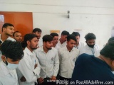 The image shows a group of young men standing in a room with white walls and orange doors. They are all wearing white lab coa...