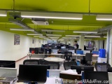 The image shows an empty office space with multiple computer desks and chairs arranged in rows. The desks are covered with wh...