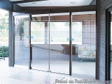 The image shows a modern entrance of a building with a large glass door. The door is made of glass and has a black frame. The...