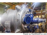 The image shows a large industrial machine in a factory. The machine is made of stainless steel and has a cylindrical shape w...