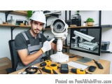 The image shows a young man wearing a white hard hat and overalls, sitting at a desk in front of a computer monitor. He is ho...
