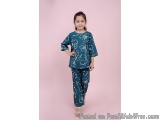 The image shows a young girl standing against a pink background. She is wearing a blue top with white floral patterns on it a...